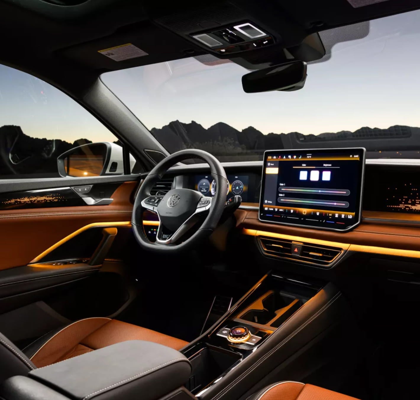 Tiguan SUV interior featuring brown leather seats, ambient lighting, a digital driver display, a large touchscreen infotainment system, and a panoramic view through the windshield at dusk.