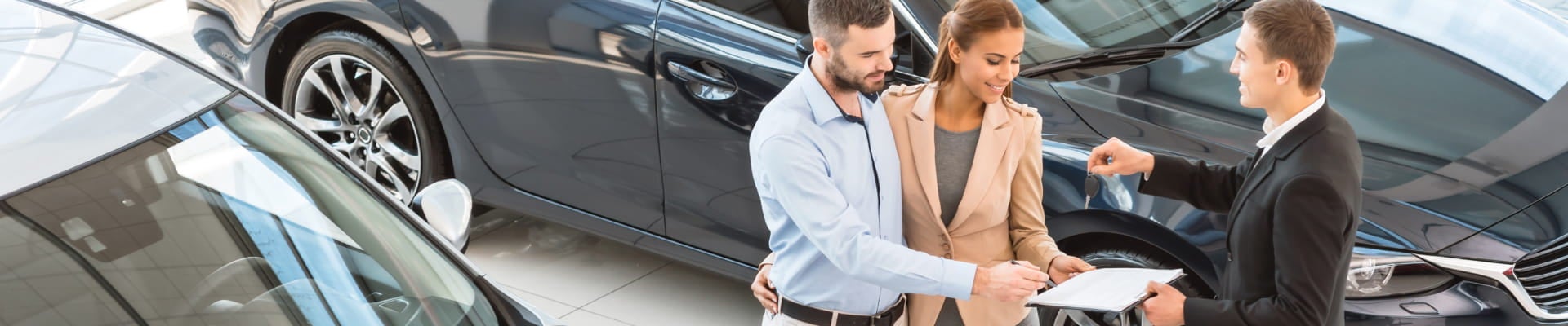 Couple reviewing paperwork with a salesperson holding car keys inside a dealership showroom.