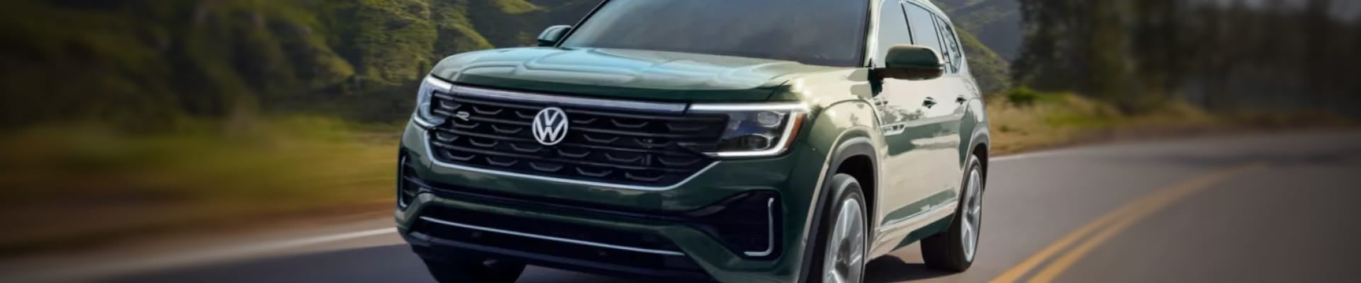 Green Volkswagen Atlas driving on a winding road surrounded by mountains.