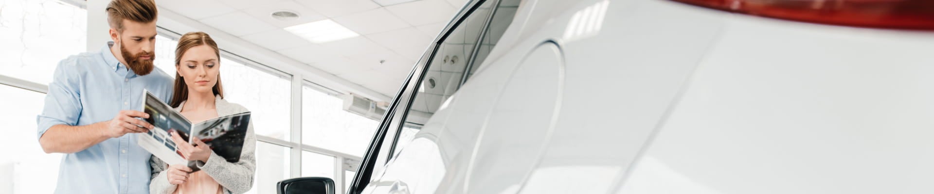 Couple reviewing a vehicle brochure beside a white SUV inside a dealership showroom.